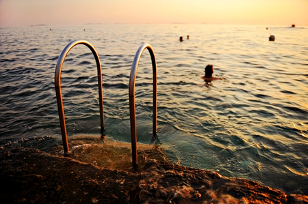 Ladder on a pontoon and people swimming in Adriatic Sea at sunsetの写真素材