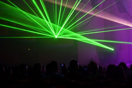 Unrecognizable people watching a beautiful laser show with multicolored lightsの写真素材