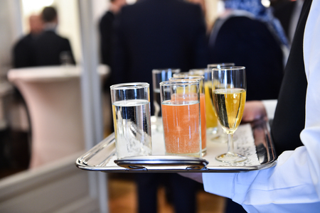 Waiter holding a tray with champagne glasses and other beverages during a cocktail eventの写真素材