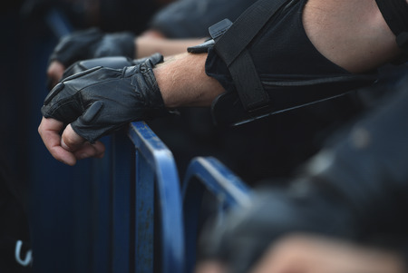 Police officer hands on a security fence during a riotの写真素材