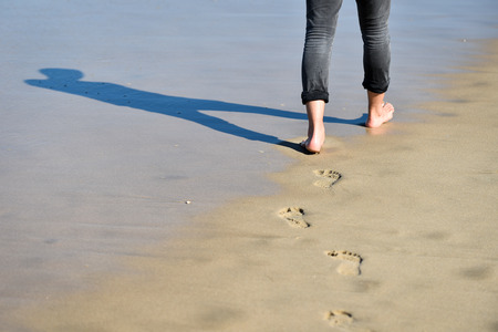 Man walking barefoot making footprints in the sand on a beachの写真素材