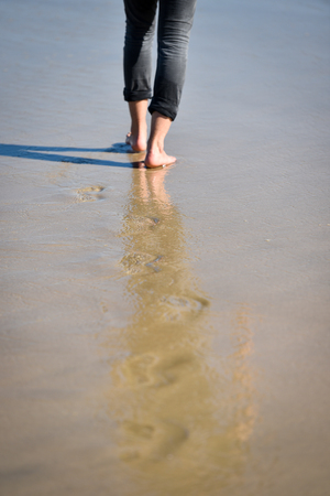 Man walking barefoot making footprints in the sand on a beachの写真素材
