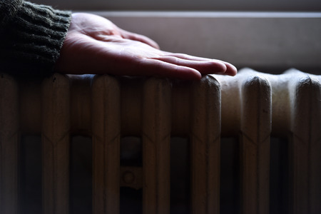 Detail with a hand checking the heat coming from a household radiator