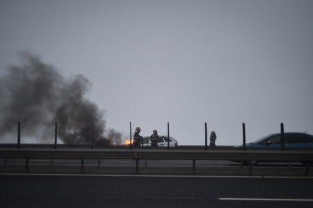 Firemen try to extinguish a burning car on a highwayの写真素材