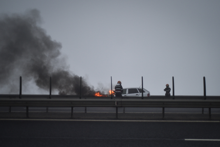 Firemen try to extinguish a burning car on a highwayの写真素材