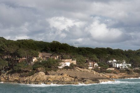 Houses in the forest at the rocks of the coast of Cala Ratjada, Mallorca, Spain. Stormy waves of the...