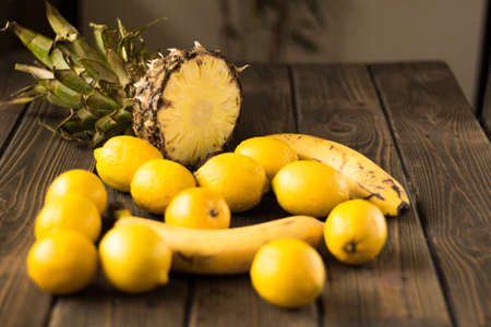 Yellow fruits. Pineapple, bananas and lemons on a wooden background.の写真素材