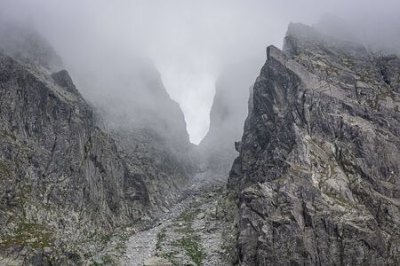 Mountain pass surrounded by fog, gray rocks in the mountains, passage between the peaks, invisible due to low clouds, in Tatra Mountainsの写真素材