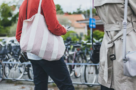 Rear view of a woman in a red jacket and black jeans holding a bag in her hands. Rear view of a...