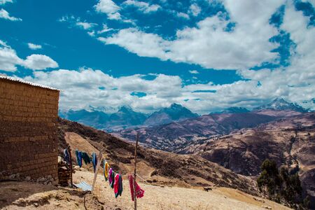 Mud house with clothes lying in the middle of a field and mountains in the background. With a blue sky full of cloudsの写真素材