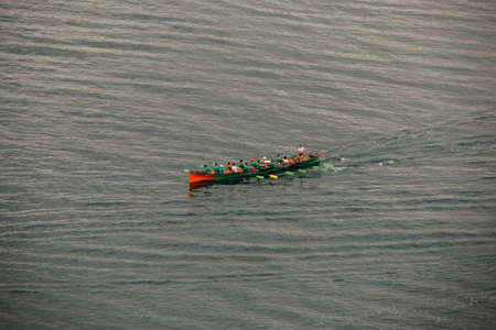 Green boat with people rowing in the sea. With shrubs in the foregroundの写真素材