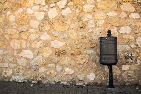 A litter bin in the street and a stone wall in the backgroundの写真素材