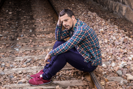 Handsome man dressed casually on the outside. Sitting on the train tracks.の写真素材