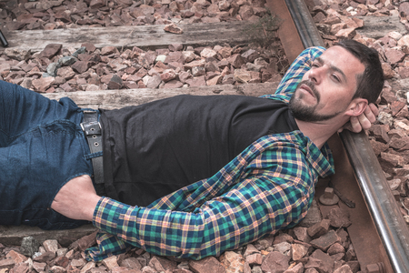 Boy with a thoughtful face and serious attitude. Picture on the train tracks, man dressed casual. Portraitの写真素材
