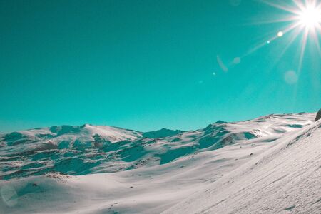 Snow-covered mountain scenery with the sun and blue skyの写真素材