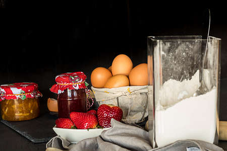 Ingredients for pancakes, jam, eggs, flour and strawberries. Dark rustic setの写真素材