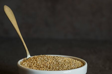 Quinoa seeds in a bowl and spoon. Healthy, protein-rich carbohydrates. Rustic and dark backgroundの写真素材
