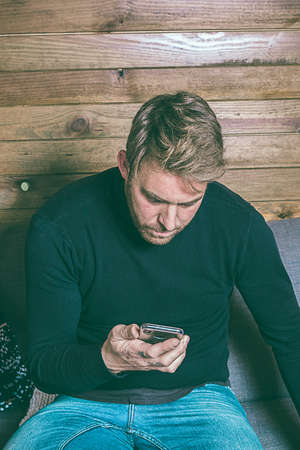 Normal guy looking at the cell phone on the couch. Dressed in casual clothes. A young, carefree lifestyle. Social network style photographyの写真素材
