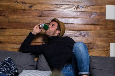 Boy in a hat drinking from a beer at home. Relaxed expressionの写真素材