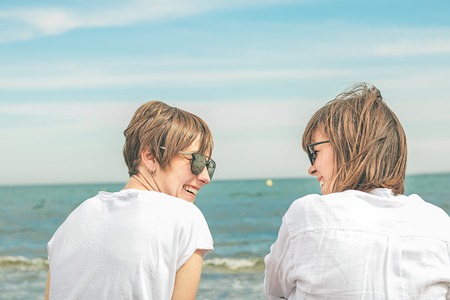 Two girls smiling, looking at each other by the sea. expression of friendship and complicityの写真素材