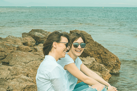 Two happy, smiling, normal girls on the beach. Sensation of joy between two friends. Dressed in white and with sunglassesの写真素材