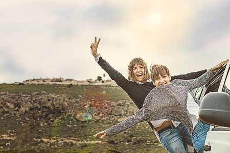 Girls at the door of a moving car with their arms up.の写真素材