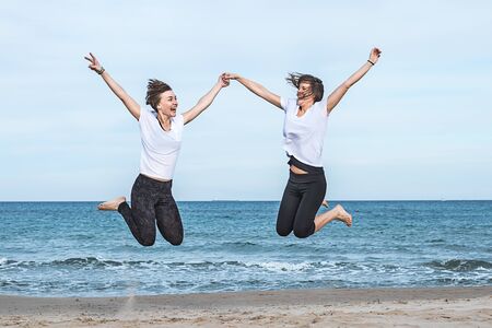 Two young girls jumping on the beachの写真素材