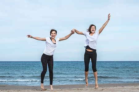 Two young girls jumping on the beachの写真素材