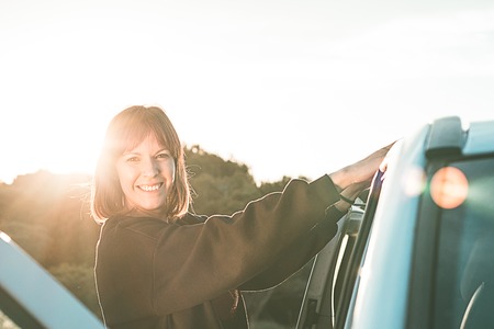 Young girl smiling, holding on to the door of a car... Concept of travel and freedomの写真素材
