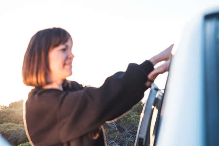 Young girl smiling, holding on to the door of a car... Concept of travel and freedomの写真素材