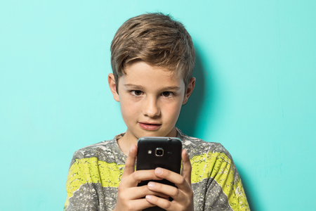 Kid looking at a cell phone with a surprised look on his face. Boy looking at his cell phoneの写真素材
