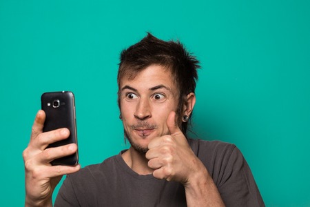 Guy making a selfie with funny faces. Guy taking pictures on his smartphone with a funny expression.