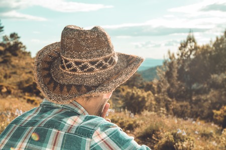 Guy in a hat and plaid shirt at sunset in the mountains. Man looking to the horizon in the mountainの写真素材