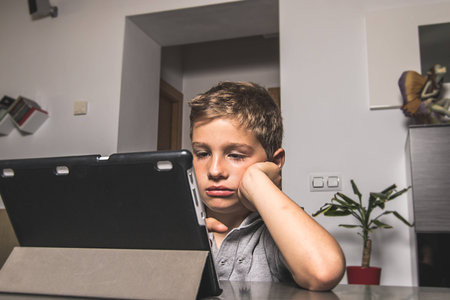 Child looking at a tablet with expression on the serious face. Close-up of a boy looking at a tablet at homeの写真素材