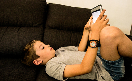 Boy on the sofa at home looking at a tablet. Kid looking at a tabletの写真素材