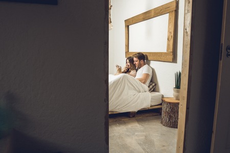 Couple of guy and girl lying in bed watching the cell phone. Man and woman looking at their cell...