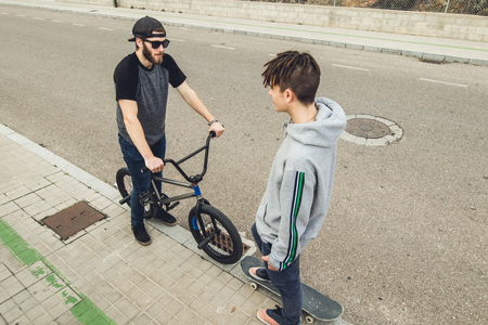 Young people greeting each other in the street. Two friends greeting each other, with a skateboard and bmx bike.の写真素材