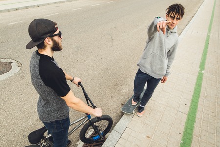 Young people greeting each other in the street. Two friends greeting each other, with a skateboard and bmx bike.の写真素材