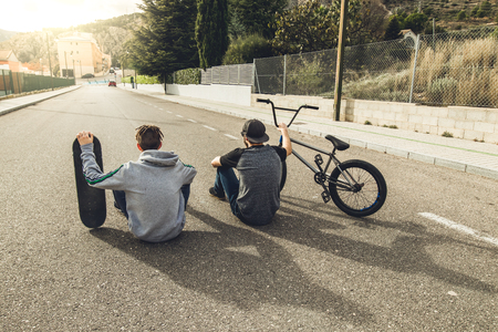 Young people riding bikes and skateboards in the city. Modern Guys with a skate and a bmx down the street.の写真素材