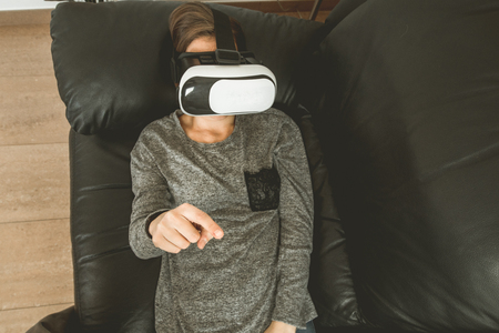 A girl with VR glasses on the couch touching with a finger. Virtual Reality Glasses Technologyの写真素材