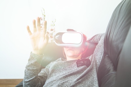 A girl with VR glasses on the couch touching with a finger. Virtual Reality Glasses Technologyの写真素材