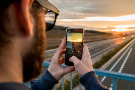 Guy taking a photo with his mobile phone at sunsetの写真素材