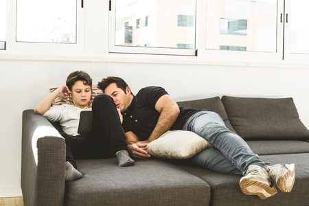 Boy with his father looking at a tablet on the couch. Concept of technology between parents and childrenの写真素材