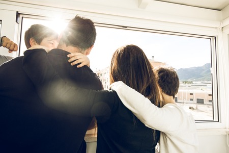 A family with kids hugging and looking out the window. Concept of a happy large familyの写真素材