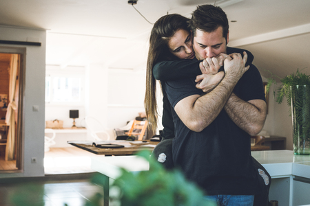 A woman hugging a man at home. Romantic concept of love and affection between couples.Young couple embracingの写真素材