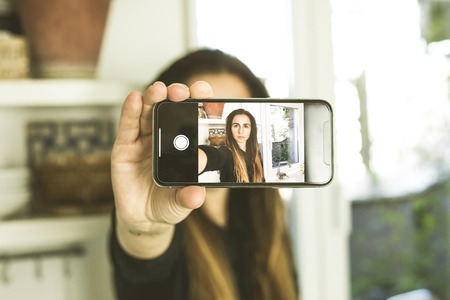 A woman making a selfi with serious expression at home.Woman taking a picture with her mobile phone.