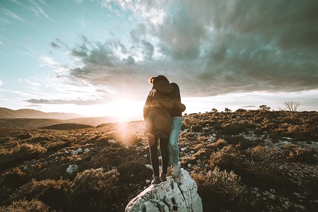 Happy couple hugging watching a sunset on the mountain. Romantic concept and love between a man and...