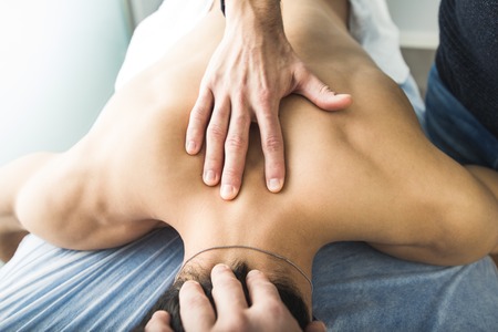 Physiotherapist massaging the back and neck of a young man. Concept of physiotherapyの写真素材