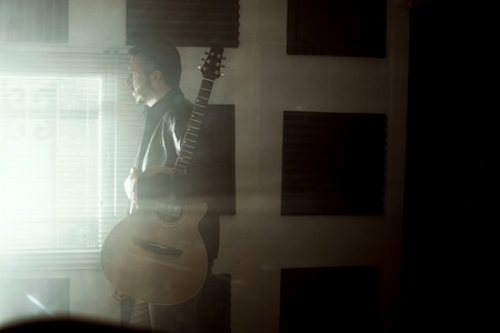 Young man with a classical guitar indoors. Dramatic portrait of a guitaristの写真素材