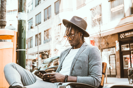 Portrait of modern African-American guy looking at the mobile phone on the street